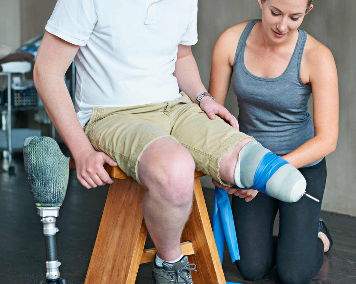 physiotherapist helping a amputated man checking his below the knee prosthesis and liner