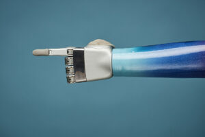 Prosthetic arm with hand pointing with the index finger against a blue background