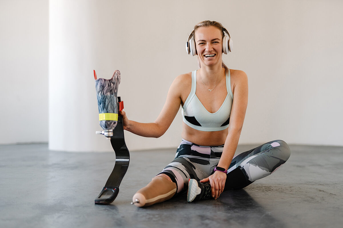 Woman sitting down on the floor holding her running blade in her hand smiling