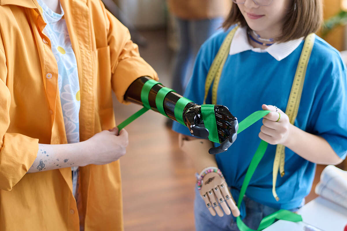 Young persons standing with ribbons, both wearing advanced arm and hand prosthesis