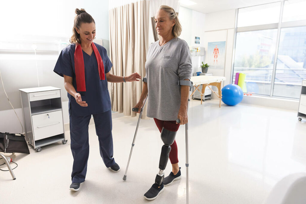 Female therapist helping an above the knee amputated patient walking with crutches