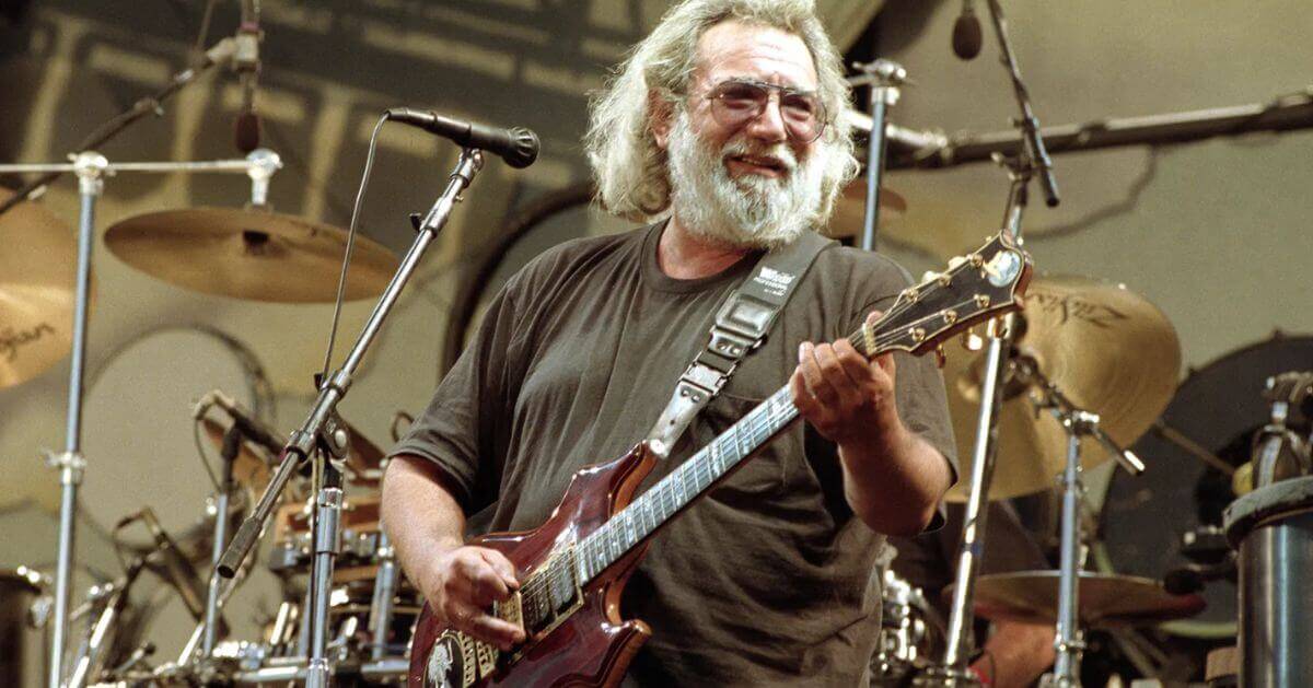 Jerry Garcia of the Grateful Dead performing live on stage, smiling as he plays his electric guitar.