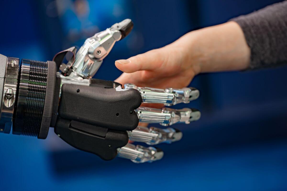 Close-up of a human hand reaching out to shake a robotic prosthetic hand.