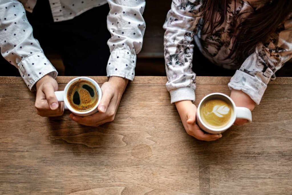 Two people (one amputee) sitting at a wooden table holding cups of coffee.