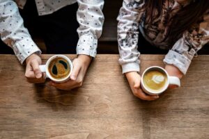 Two people (one amputee) sitting at a wooden table holding cups of coffee.