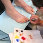 A prosthetist carefully paints details on a silicone prosthetic toe, matching the natural skin tone and creating realistic details for a lifelike appearance. Photo credits to Medical Art Prosthetics
