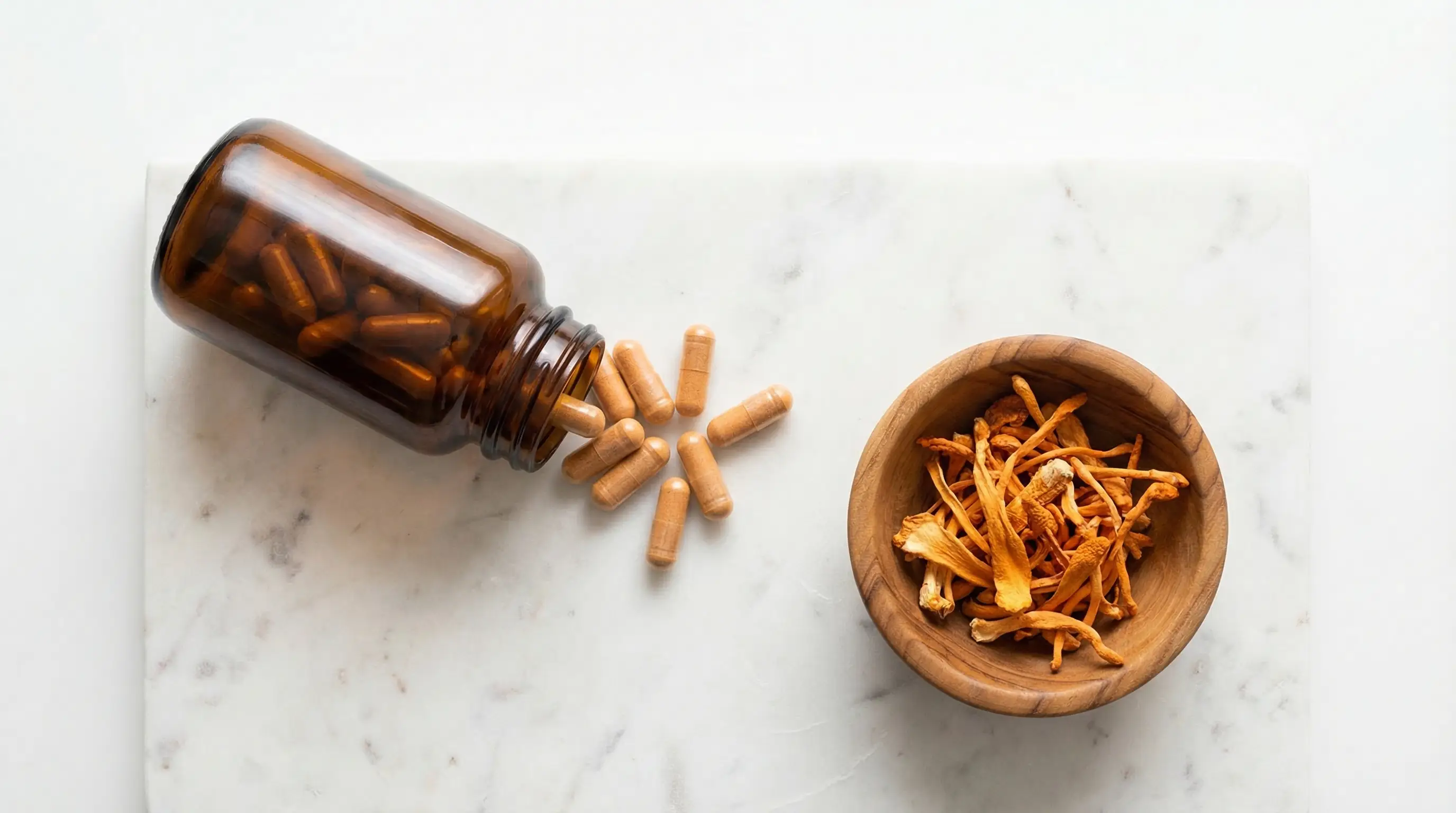 Cordyceps supplement capsules spilling from amber bottle next to dried cordyceps mushrooms