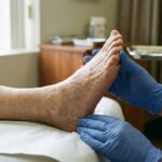 Clinician in gloves examining an older adult bare foot and toes during a clinic exam