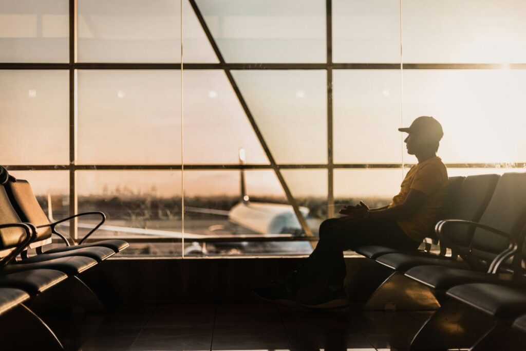 Silhouette of a person sitting alone in an empty airport terminal, with rows of seats.