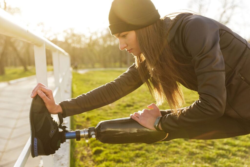 Person with a below-knee prosthetic leg stretching outdoors before exercise on a sunny day.