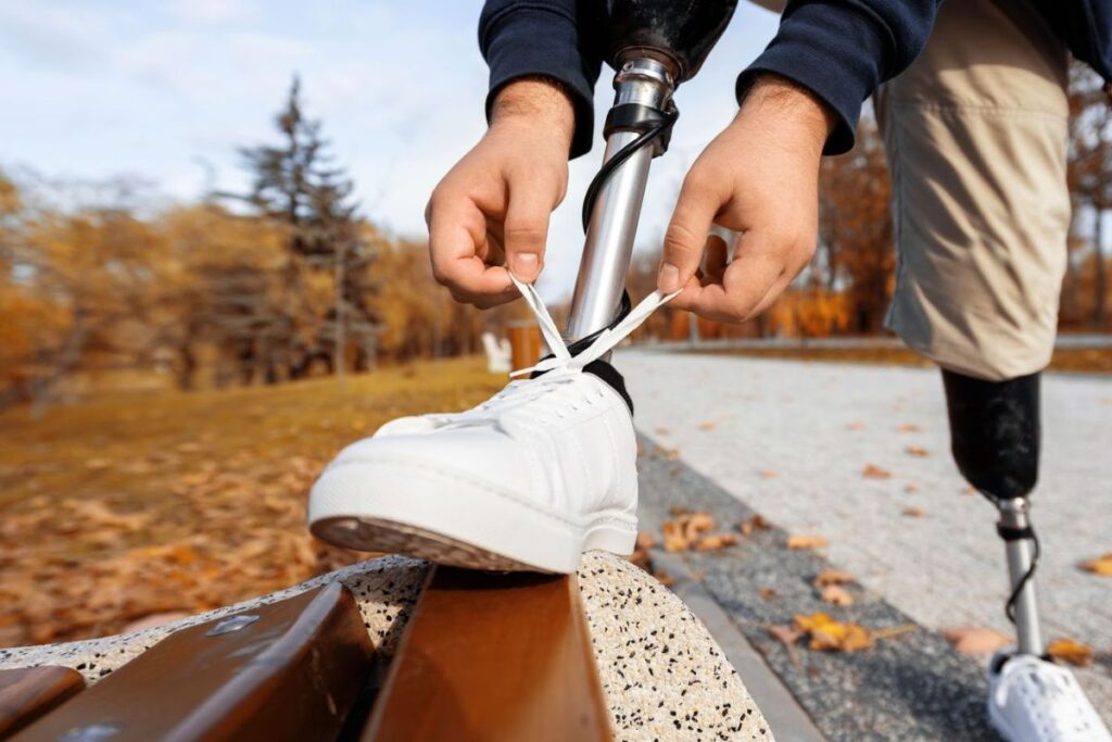 Person with a below-knee prosthetic leg tying a sneaker outdoors before a walk.