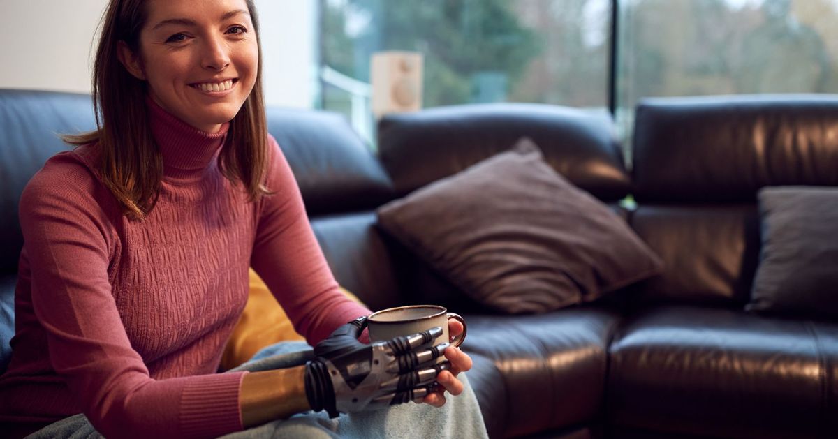 Person with a myoelectric prosthetic hand holding a coffee mug at home.