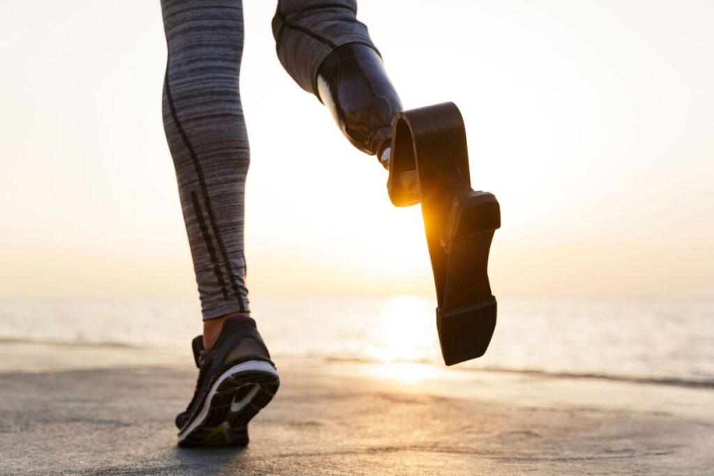 Person walking with a below-knee running prosthetic leg along the beach.