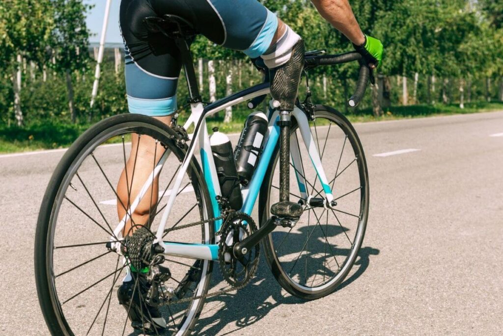 Cyclist riding a road bike with an above-knee prosthetic leg on an outdoor road.