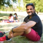 Person with a prosthetic leg sitting in a park with family in the background on a sunny day.