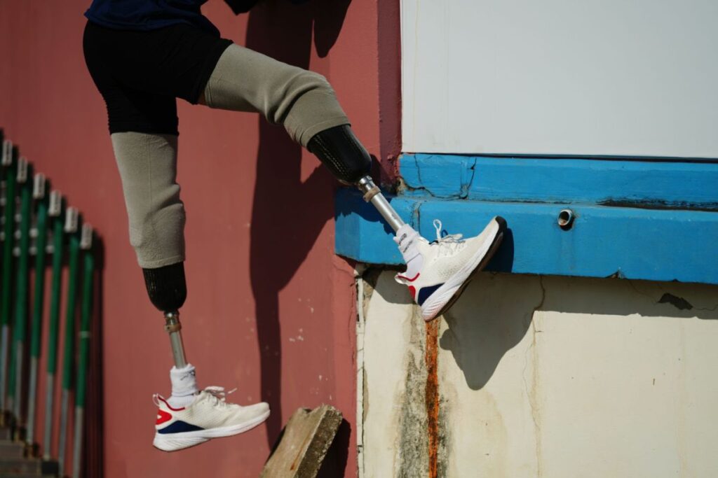 Bilateral below-knee amputee wearing prosthetic legs and sneakers while climbing over a wall.