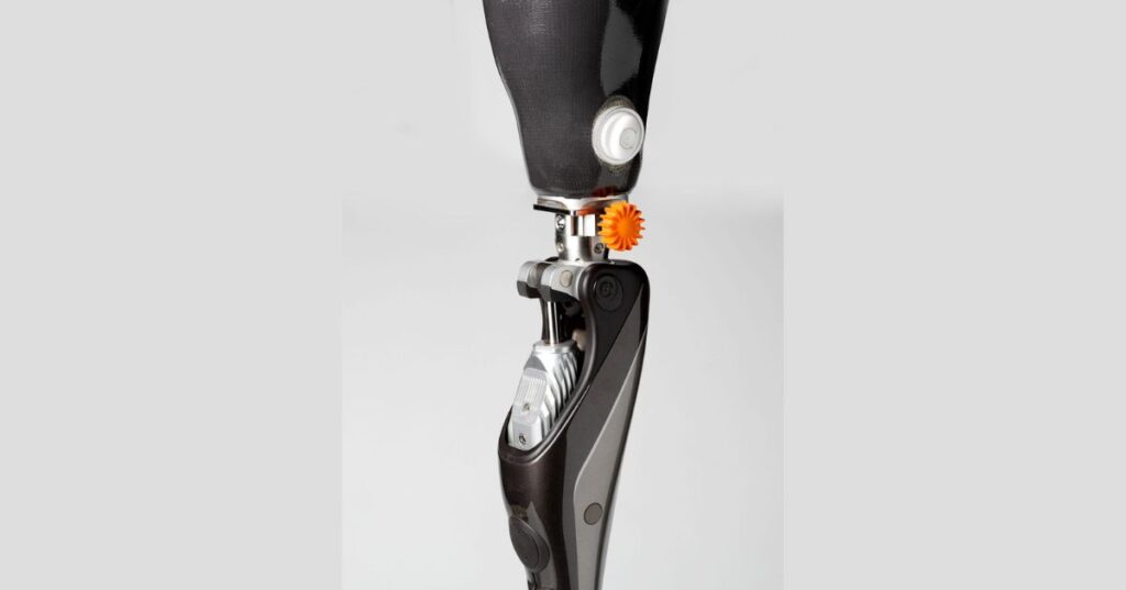 Prosthetic knee connected to a prosthetic socket with a Lindhe Quick-Change Adapter and orange locking wheel.