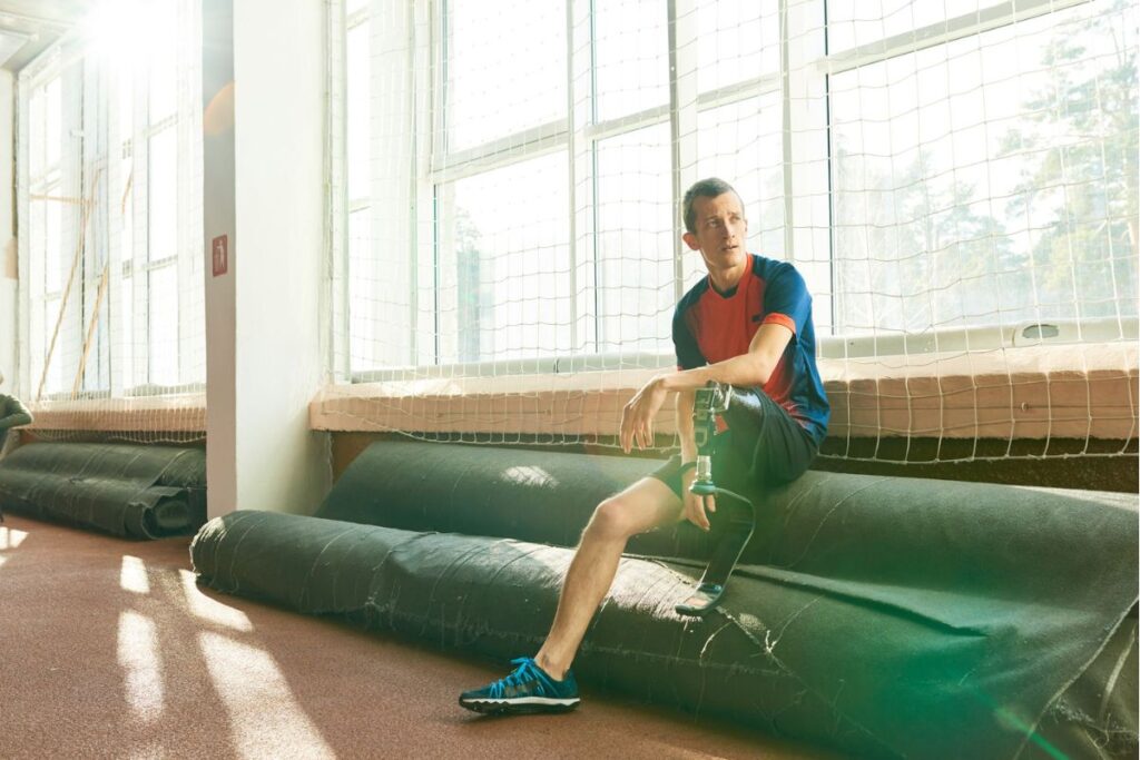 Man with a prosthetic leg resting after exercise at an indoor gym.