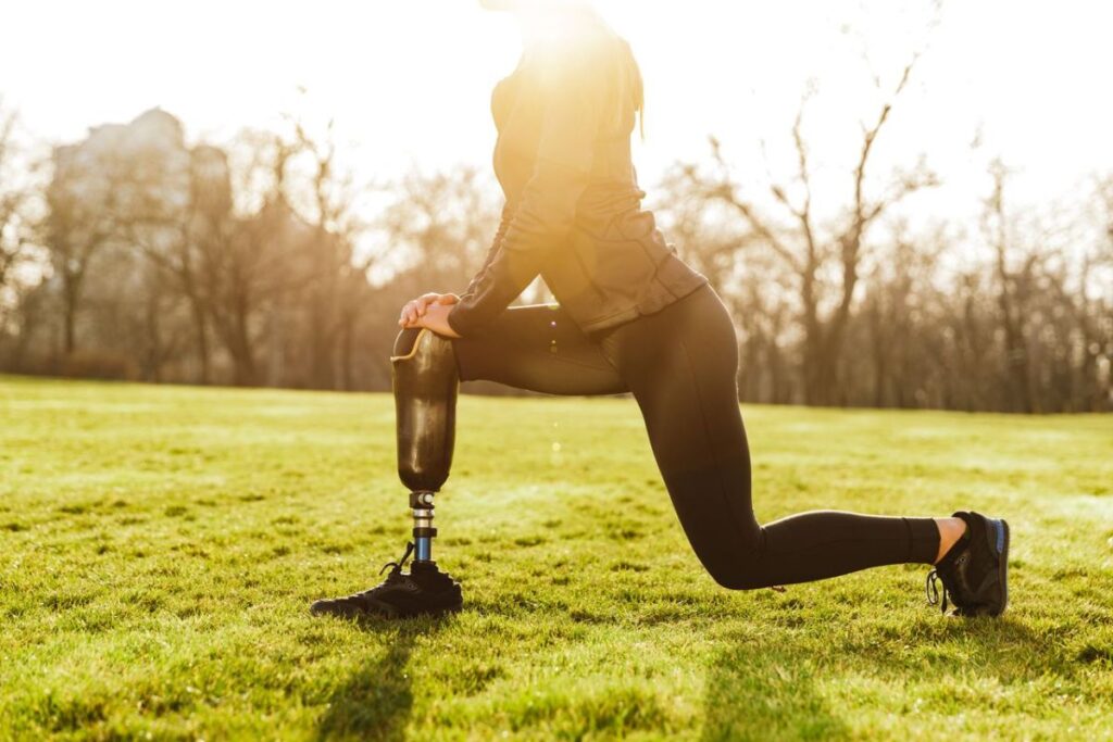 Woman with a prosthetic leg stretching outdoors on grass.