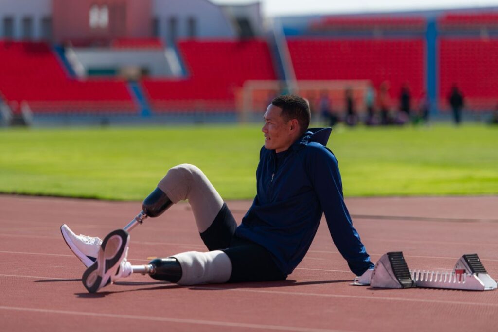 Bilateral below-knee amputee athlete wearing prosthetic legs while sitting on a running track.